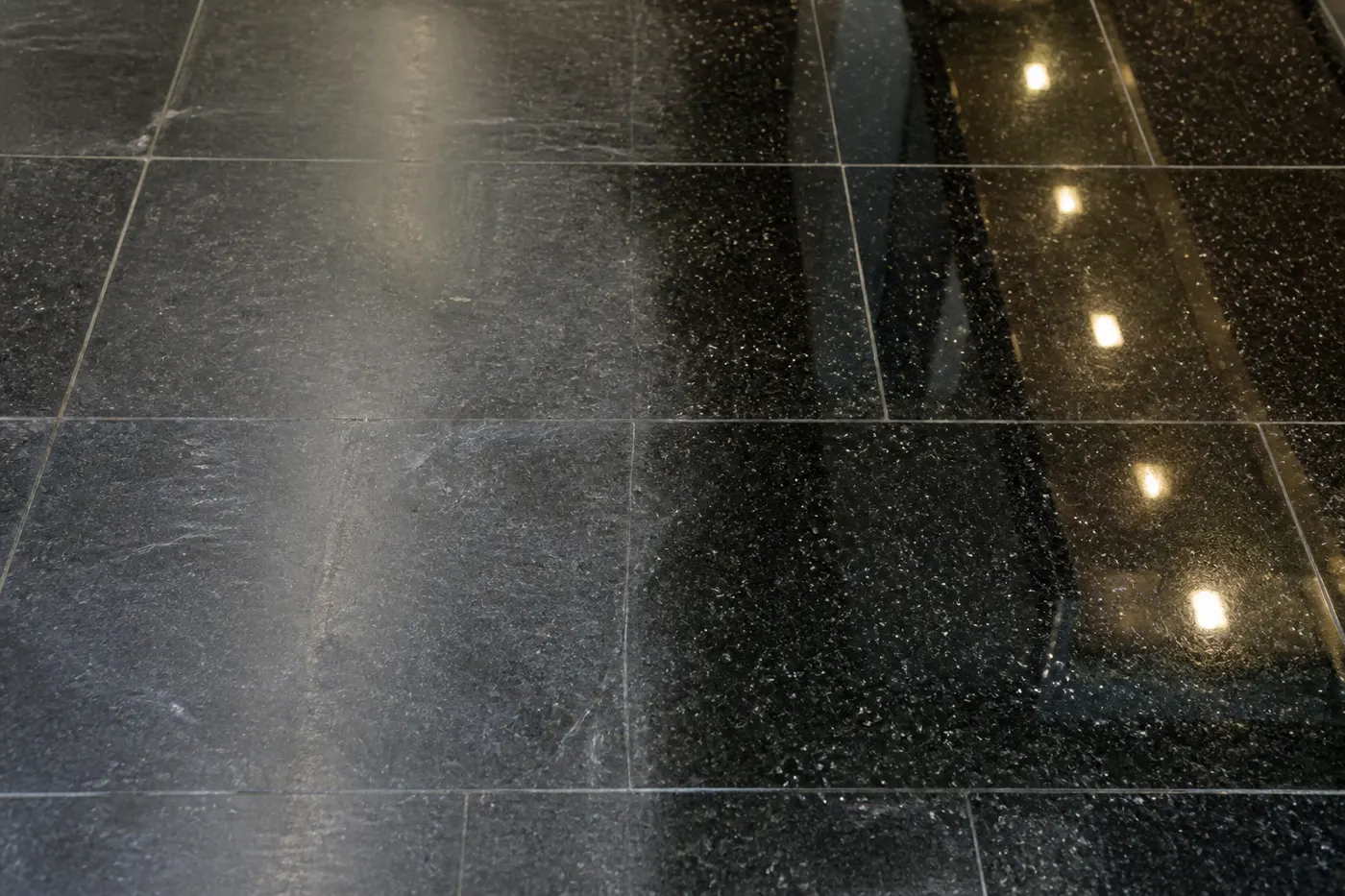 Piso de granito negro pulido y cristalizado reflejando las luces del ambiente